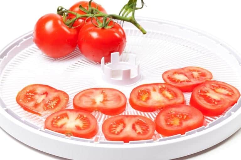 sliced tomatoes on a dehydrator tray with full tomatoes next to it