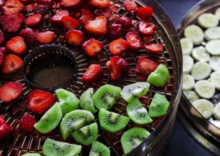 sliced kiwis, bananas, strawberries in a dehydrator tray
