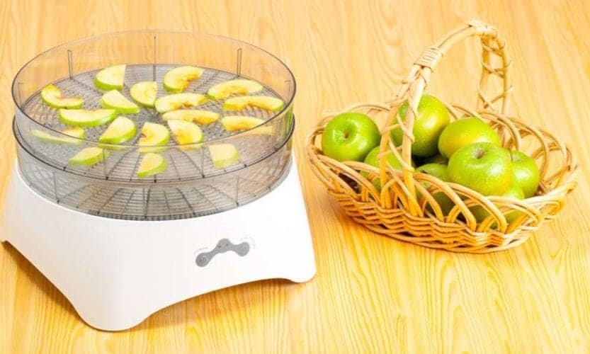 food dehydrator with slices of apple in trays next to basket full of green apples