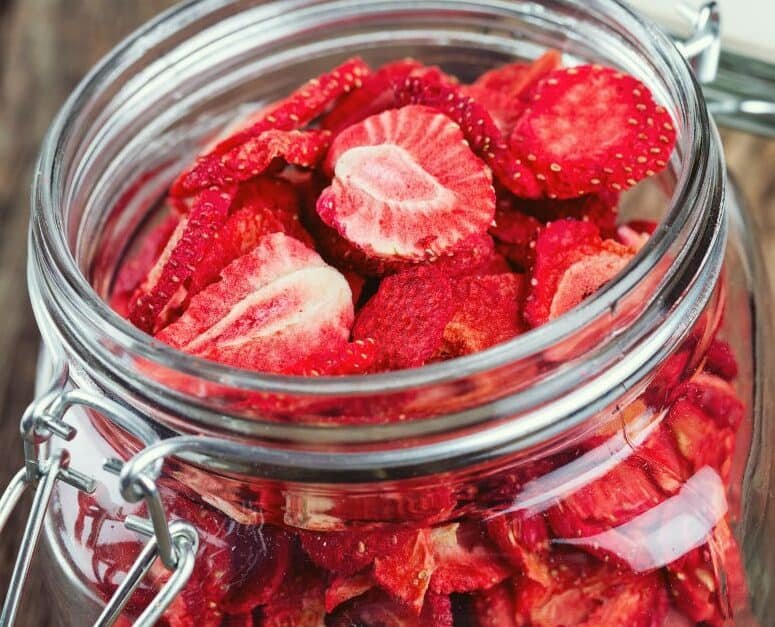 sliced dried strawberries in a glass jar on a wooden background