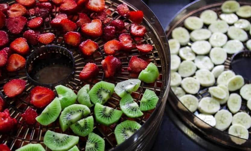 sliced strawberries and sliced kiwis on a tray next to sliced bananas on a dehydrator tray