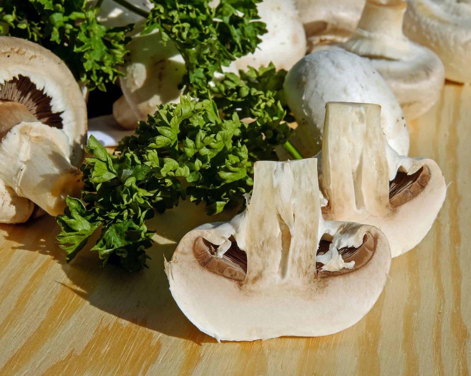 sliced mushroom with whole mushrooms and herb on a wooden backdrop