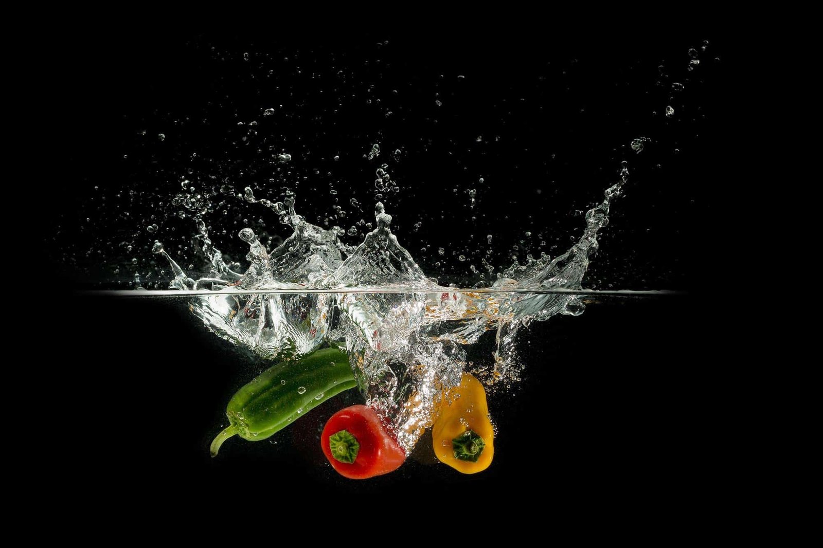 peppers thrown into water causing a splash with a black backdrop