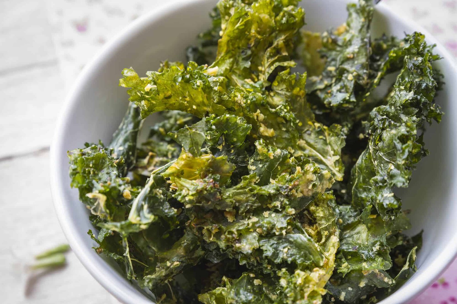 kale chips in a ceramic bowl on a backdrop of wooden table