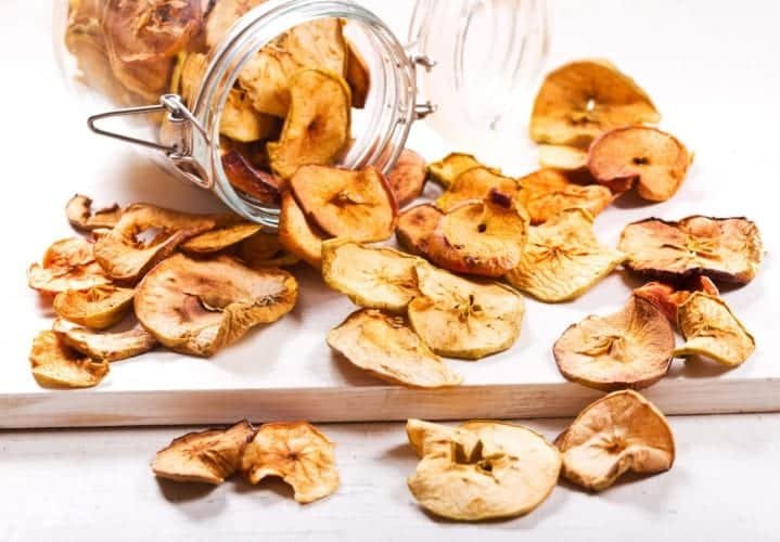 apple chips in a jar tipped over on a wooden board with a white background