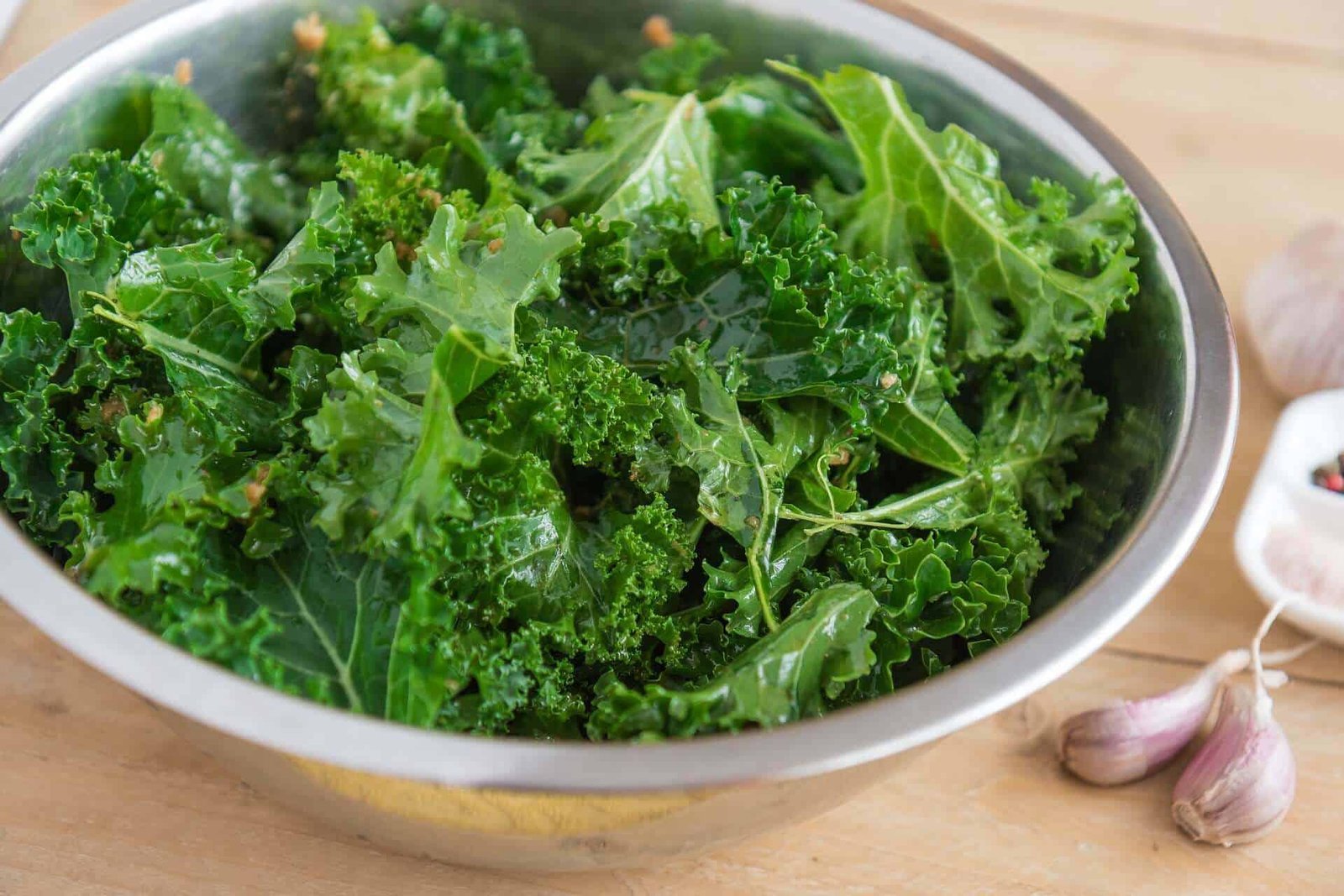 metal bowl full of kale with garlic next to it on a wooden backdrop