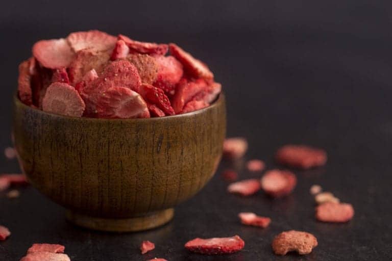 dried strawberries in small wooden bowl and around the bowl on a black background