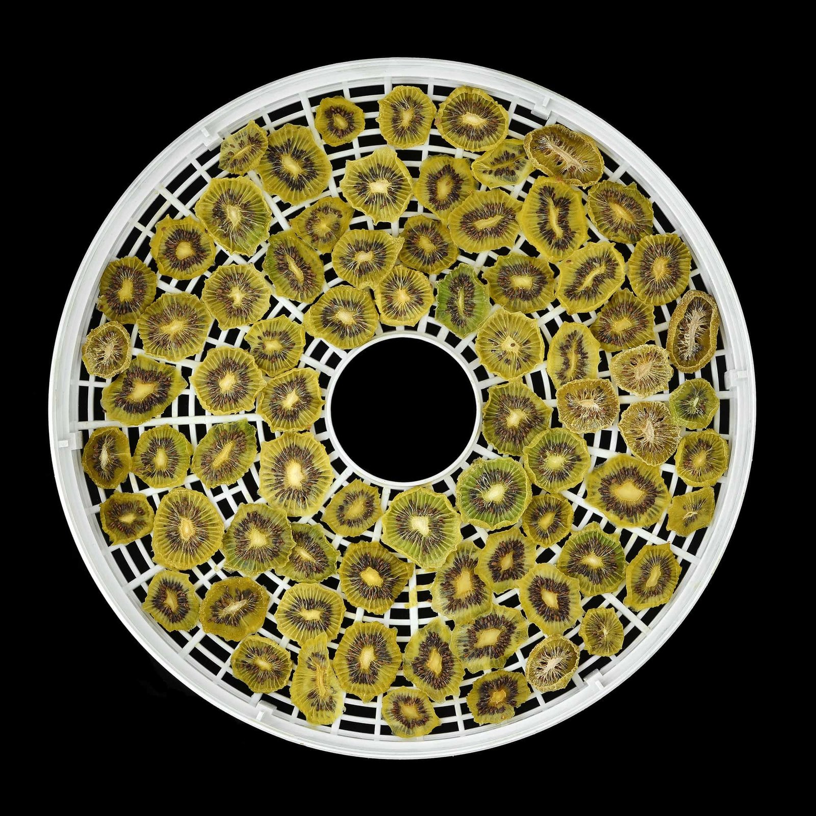 dehydrated kiwis in a circle dehydrator tray over a black background