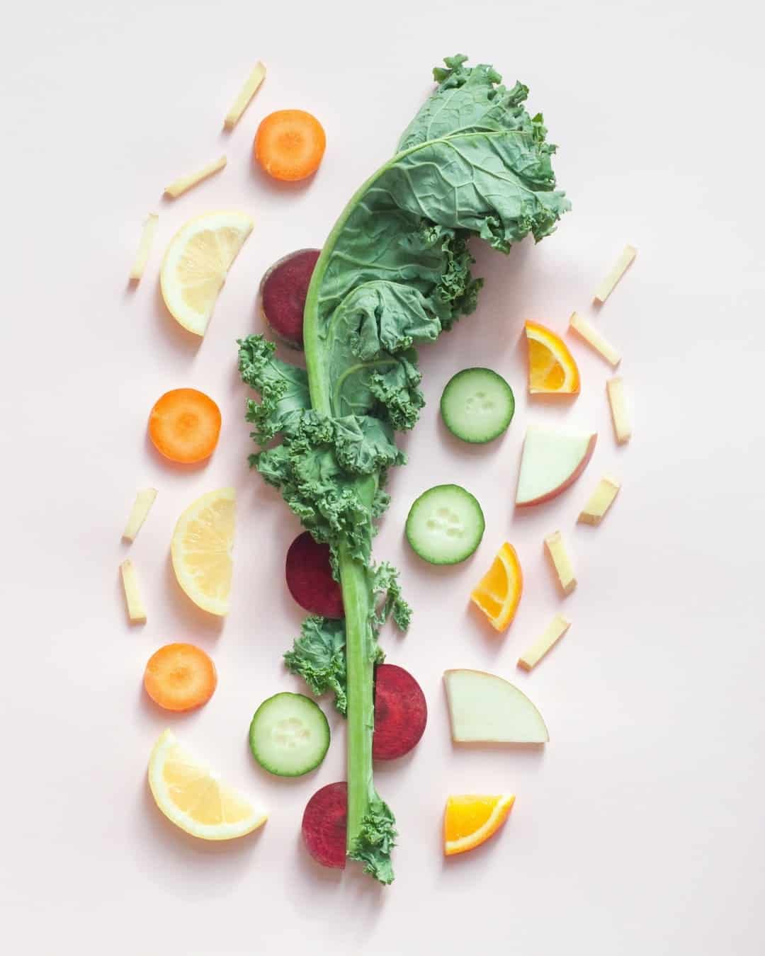 sliced orange, carrot, beetroot, apple with one kale leaf on top with white backdrop