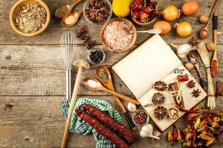 blank book with foods around it on a wooden table with spoons, whisk and dish towel