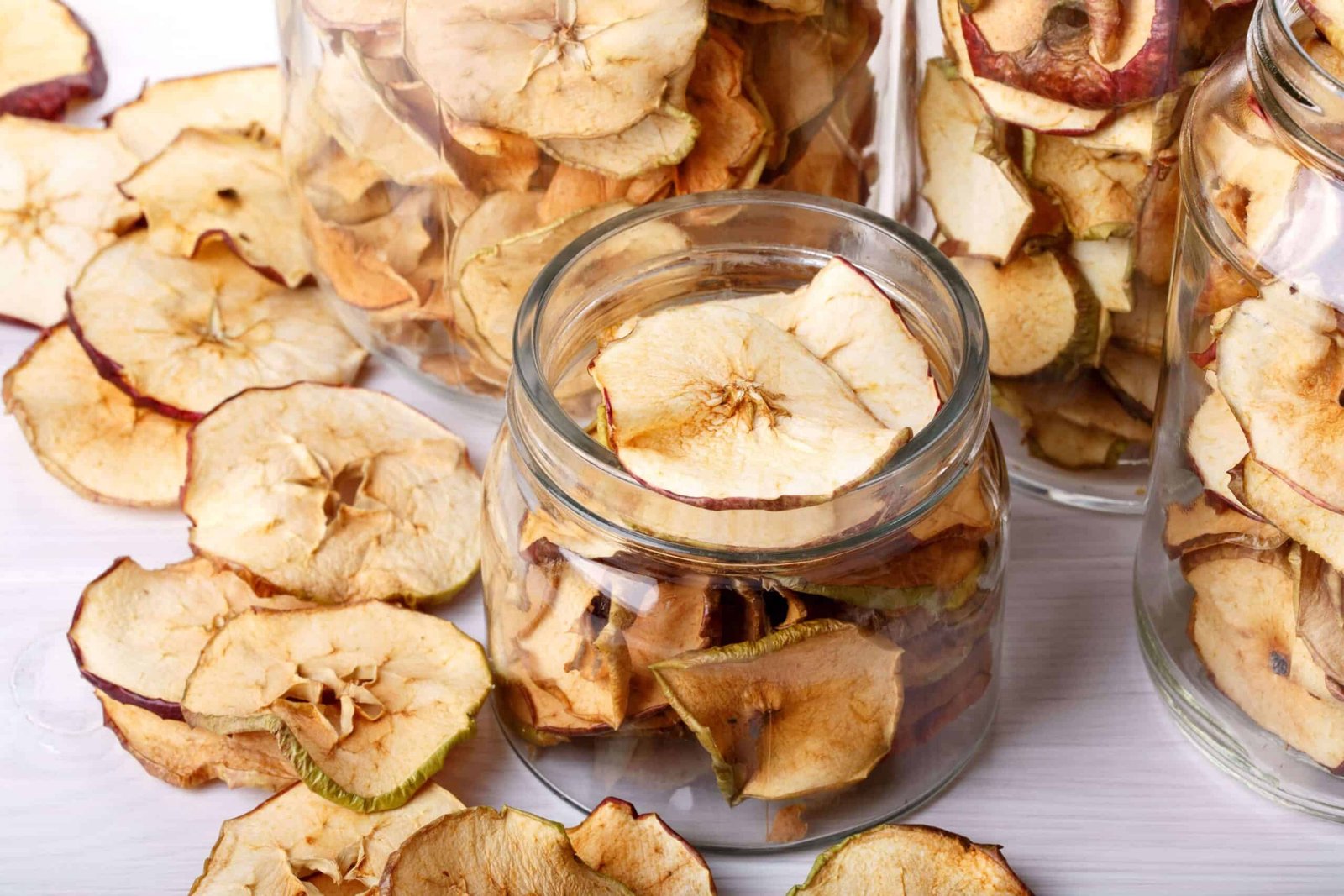 apple chips in glass jars and on white wooden table