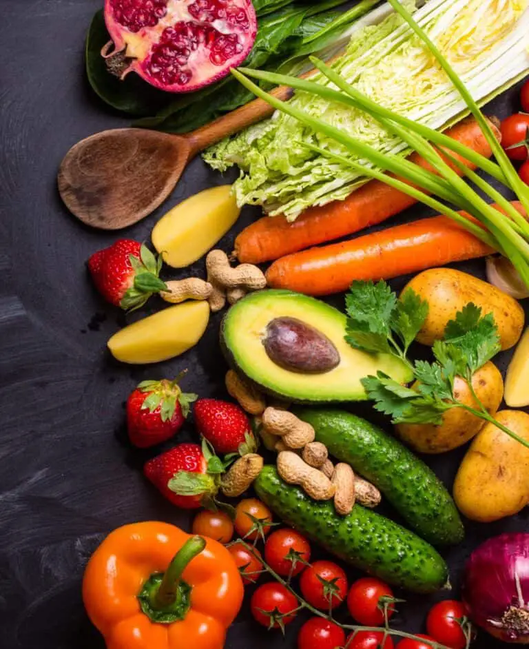 Vegetables, fruits, herbs, raw ingredients for cooking and spoon on rustic black chalk board background.