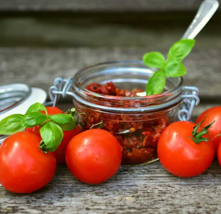 sundried tomatoes in jar and fresh tomatoes on wooden table