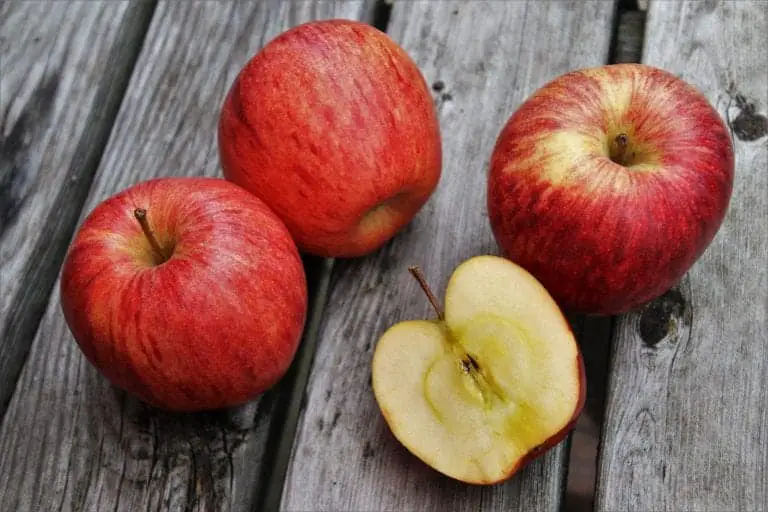 one sliced apple and three whole apples on wood table