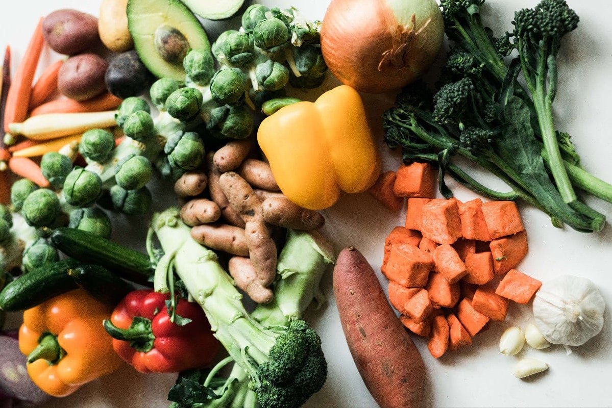 assortment of vegetables, yellow pepper, sweet potato, avocado, brocolli,onion ona white backdrop