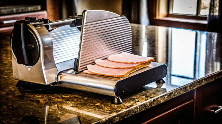 A sleek Beswood 10 Premium Meat Slicer on a modern kitchen countertop. The slicer is shown with thin, even slices of ham and cheese neatly arranged beside it, highlighting its precision and professional-grade quality.