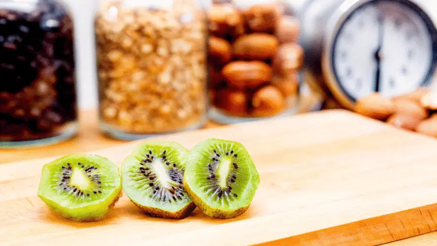 Three sliced kiwis on a wooden chopping board.