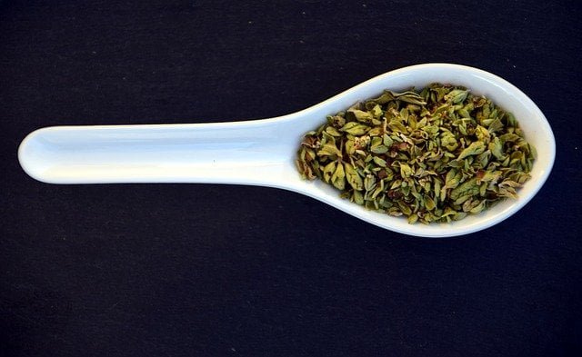 oregano seasoning close up green aromatic fragrant, oregano in plastic spoon on black background