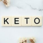the word keto on a mwhite marble background with white flowers around image