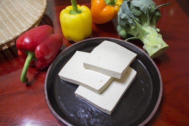 sliced tofu in sqaures on ceramic plate next to bell peppers