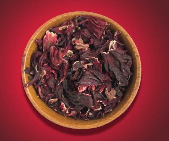 dried hibiscus flowers in wooden bowl on red background.