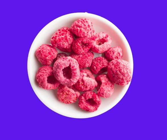 freeze dried strawberries in white ceramic plate on purple background.