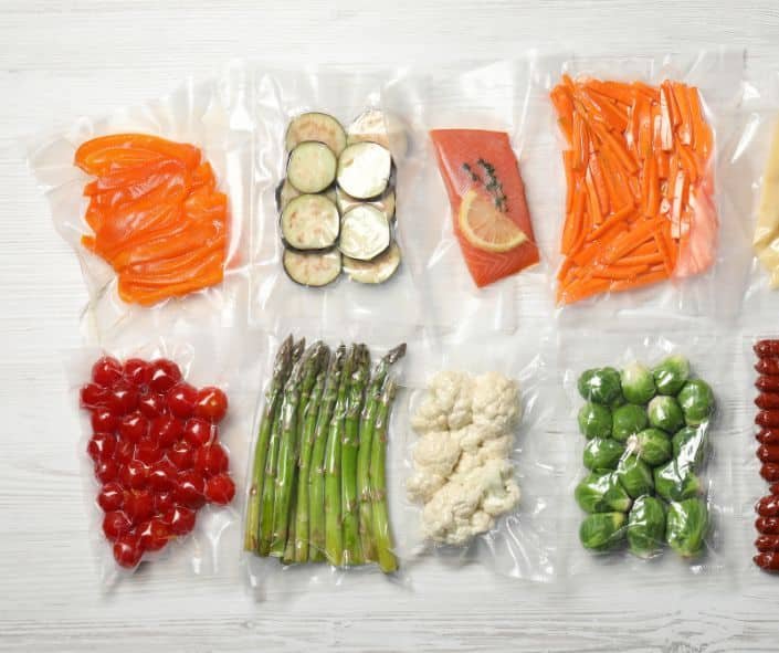 Different food products in vacuum sealed bags on white wooden table flat.