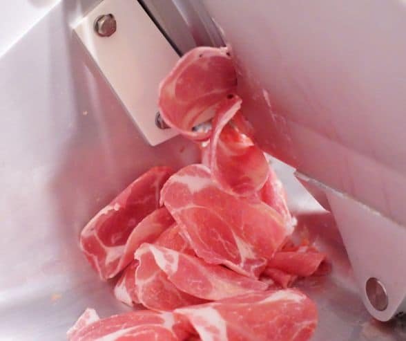meat being sliced in a meat slicer