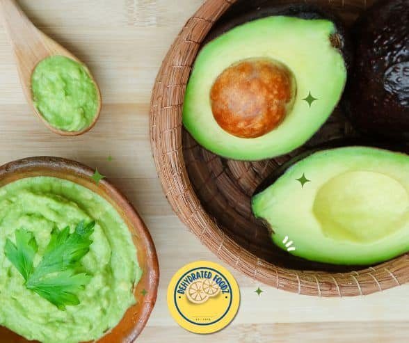 avocado sliced with pit inside on a wooden bowl, guacomole in a wooden bowl next to a spoon.