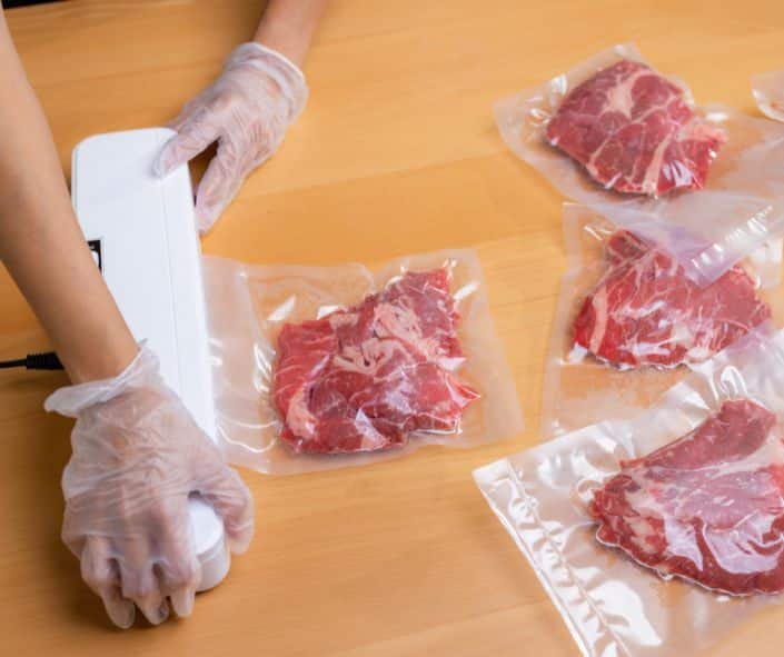 person with plastic gloves using a vacuum sealer to vacuum seal beef.