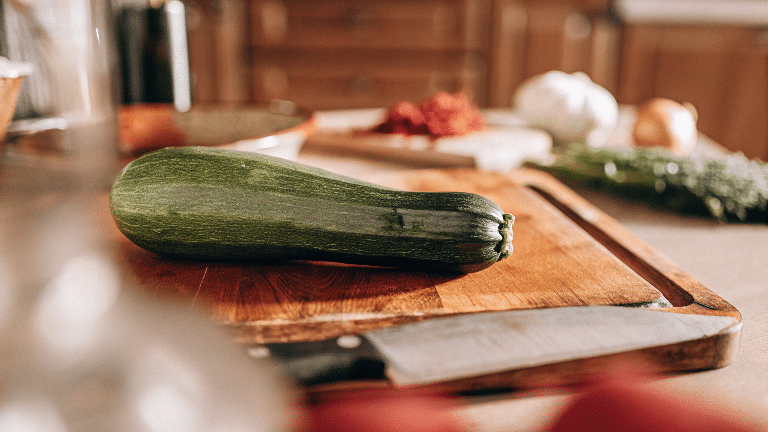 Large zucchini on a chopping board next to a kitchen.