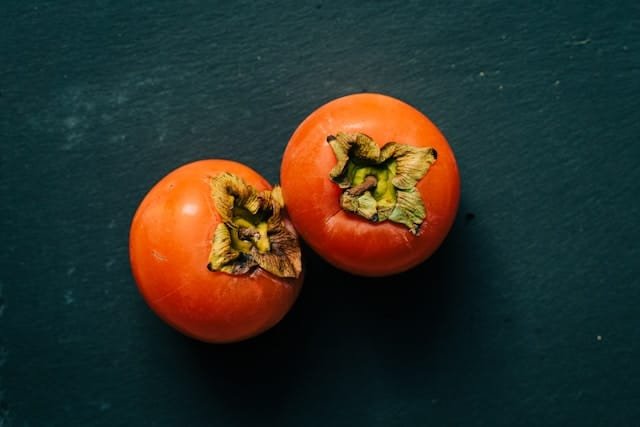 Two whole persimmons on a dark grey background.