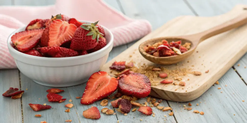 A photo of a still life featuring a culinary scene with a focus on a bowl of fresh strawberries and a wooden spoonful of granola-like mixture. The strawberries have a vibrant red color, and the granola has a mix of various textures. The background is a blurred wooden surface, and the overall setting is rustic and homey. The focus is on the ingredients and the textures of the food items, with a shallow depth of field.