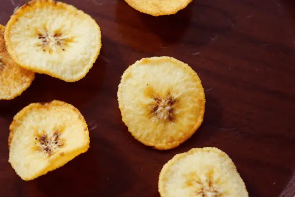 A top down closeup view of banana chips on a wooden table.