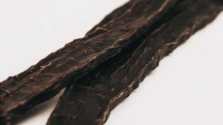 Thin dark beef jerky on a white background.