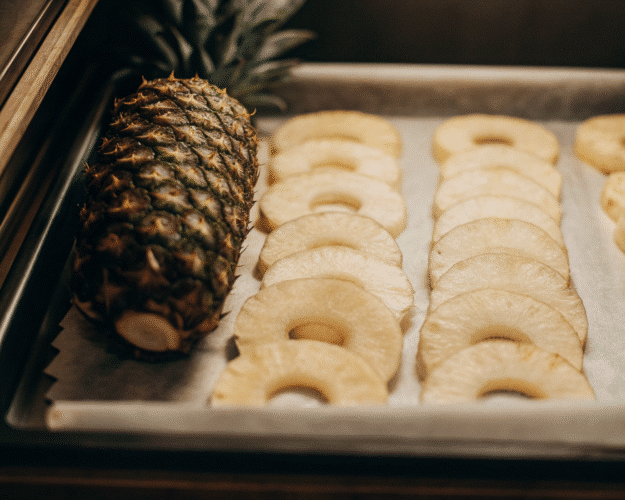 A whole pineapple next to sliced pineapple rings on a baking sheet.