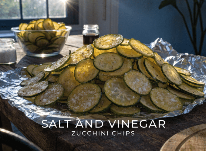 Pile of salt-and-vinegar zucchini chips on a foil-lined tray, sunlit in a kitchen.