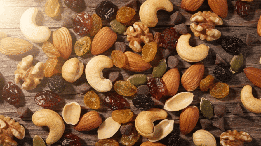 A colorful assortment of homemade trail mix is displayed, featuring a blend of nuts, seeds, dried fruit like cranberries and apricots, and dark chocolate chips. This nutritious snack mix is rich in healthy fats and protein, making it a great option for energy on a hiking trip.