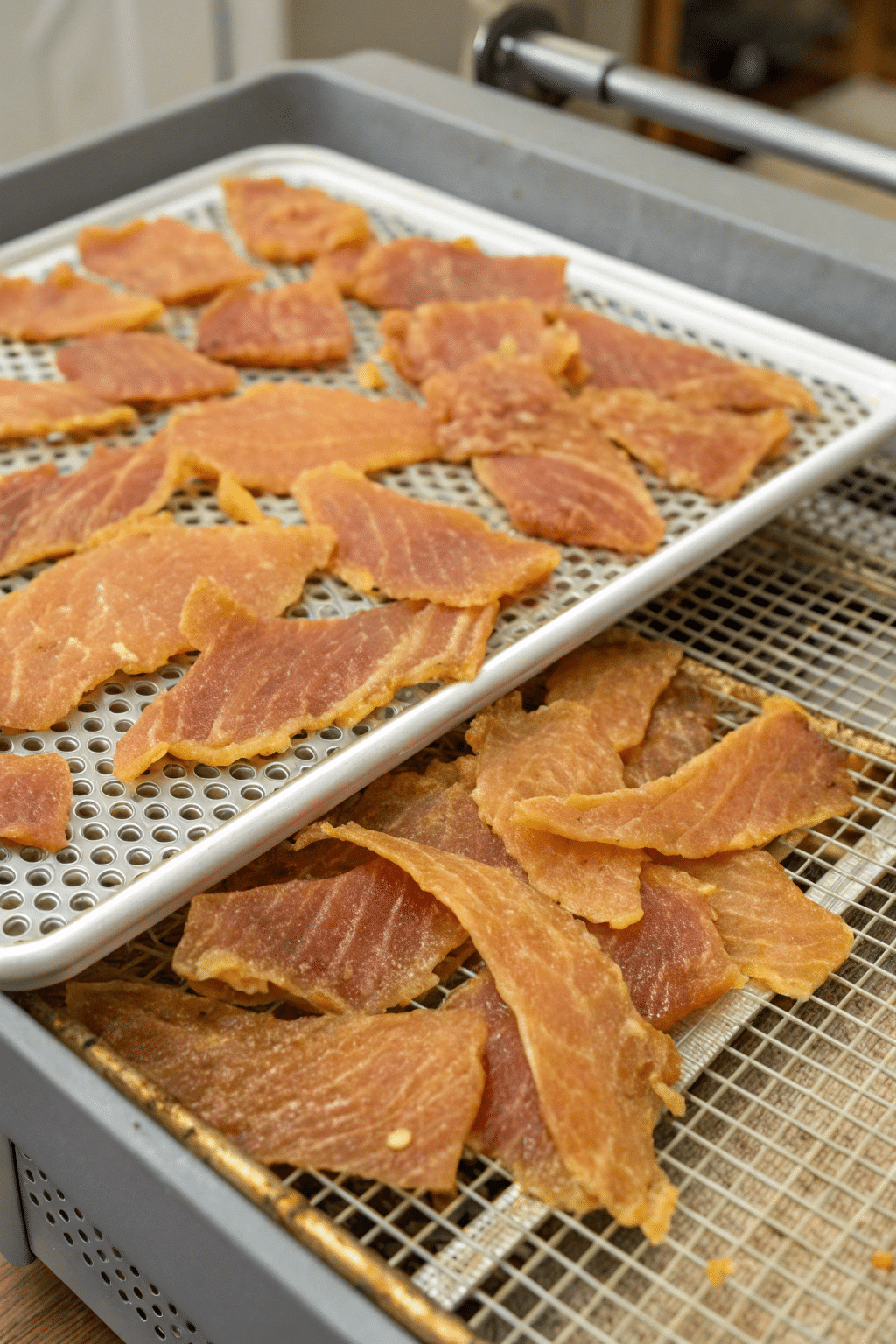 Thin slices of chicken jerky laid out on a dehydrator tray, showing the golden-brown color and dry texture of the finished treats.