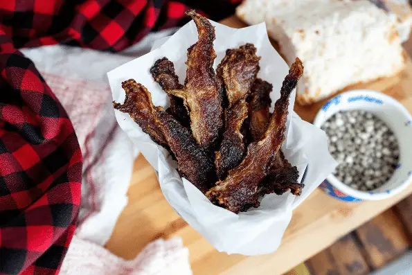 A person holding a bunch of deer jerky slices in a paper as a snack.