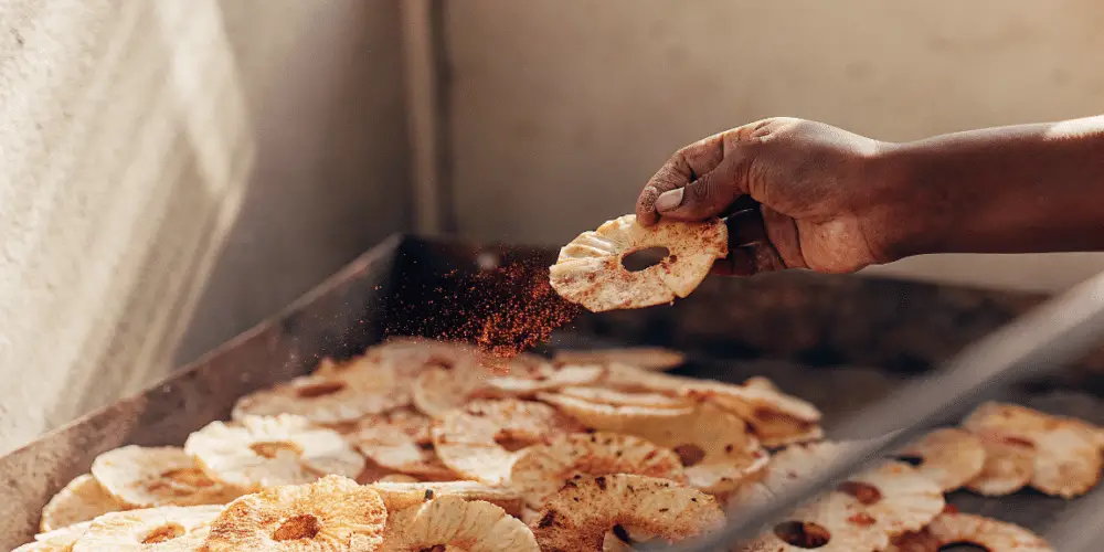 A person picking up a single spicy dehydrate pineapple rings with seasoning