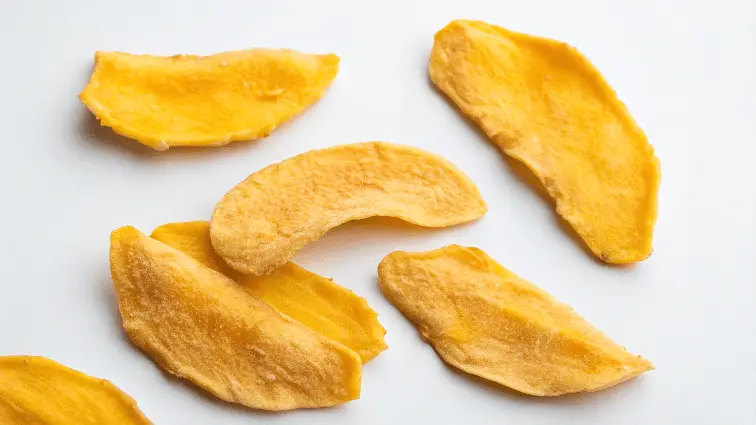A close-up image of several pieces of freeze-dried mango on a clean white background.