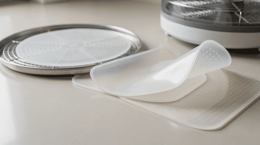 The image features a set of silicone dehydrator sheets designed to fit perfectly in food dehydrator trays, showcasing their flexibility and easy clean properties. These reusable mats protect the trays while dehydrating fruits, vegetables, and herbs, making the process of creating dried snacks like fruit leather and jerky more efficient and mess-free.